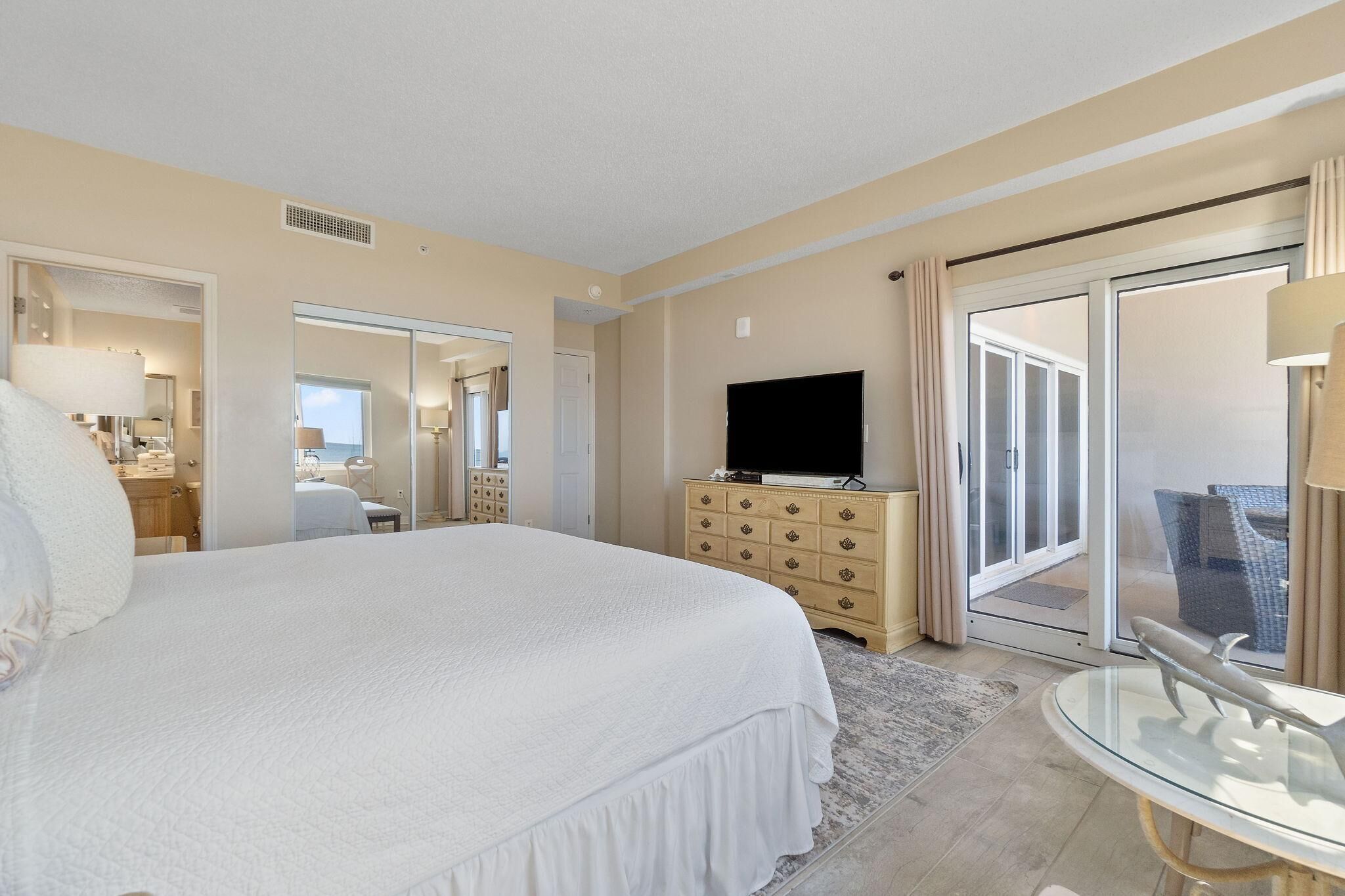 Une chambre d’hôtel avec un grand lit, une télévision, une commode et une porte-fenêtre coulissante donnant sur un balcon.