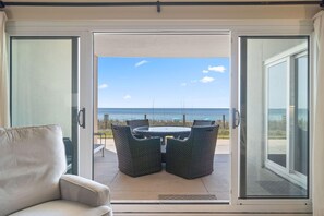 A sliding glass door leading to an outdoor seating area with a table and chairs, overlooking a beach. - Sandy Key 112 (Pensacola)