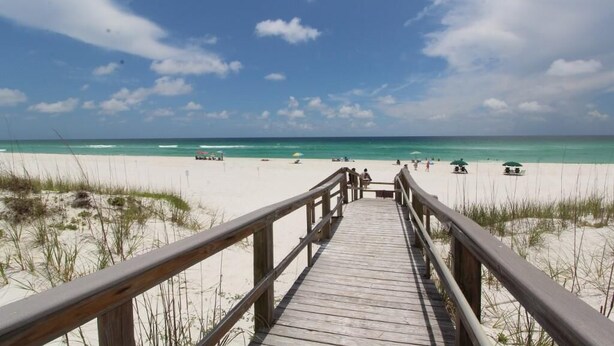 A wooden boardwalk leading to a beach with clear skies and calm waters. - Boardwalk F3 (Pensacola Beach)