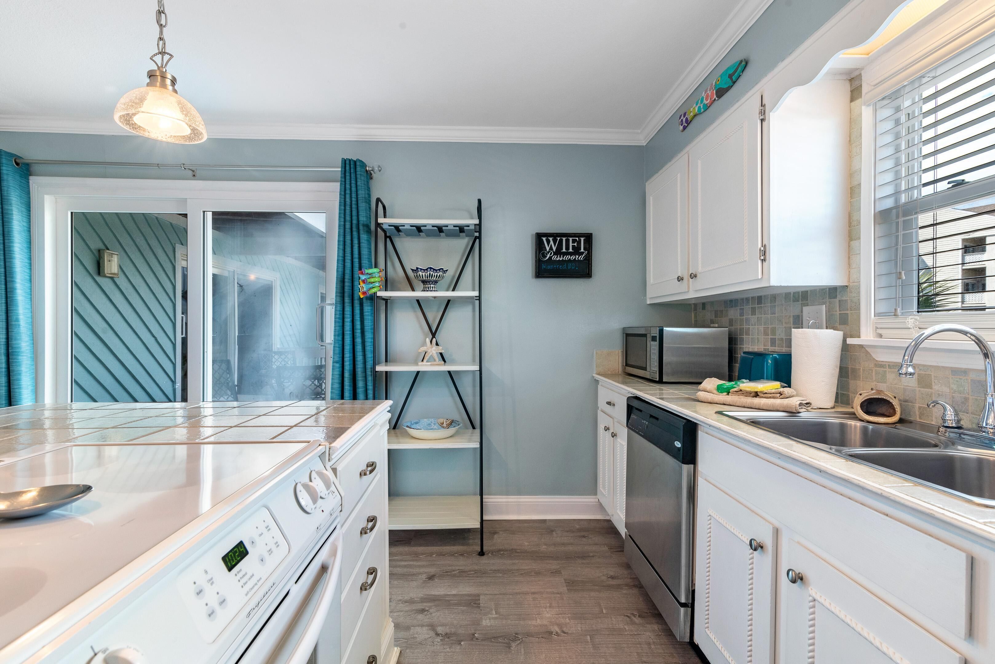 A modern kitchen with white cabinetry, a built-in oven, and a microwave. There is a shelf with decorative items and a sign indicating a WiFi password.