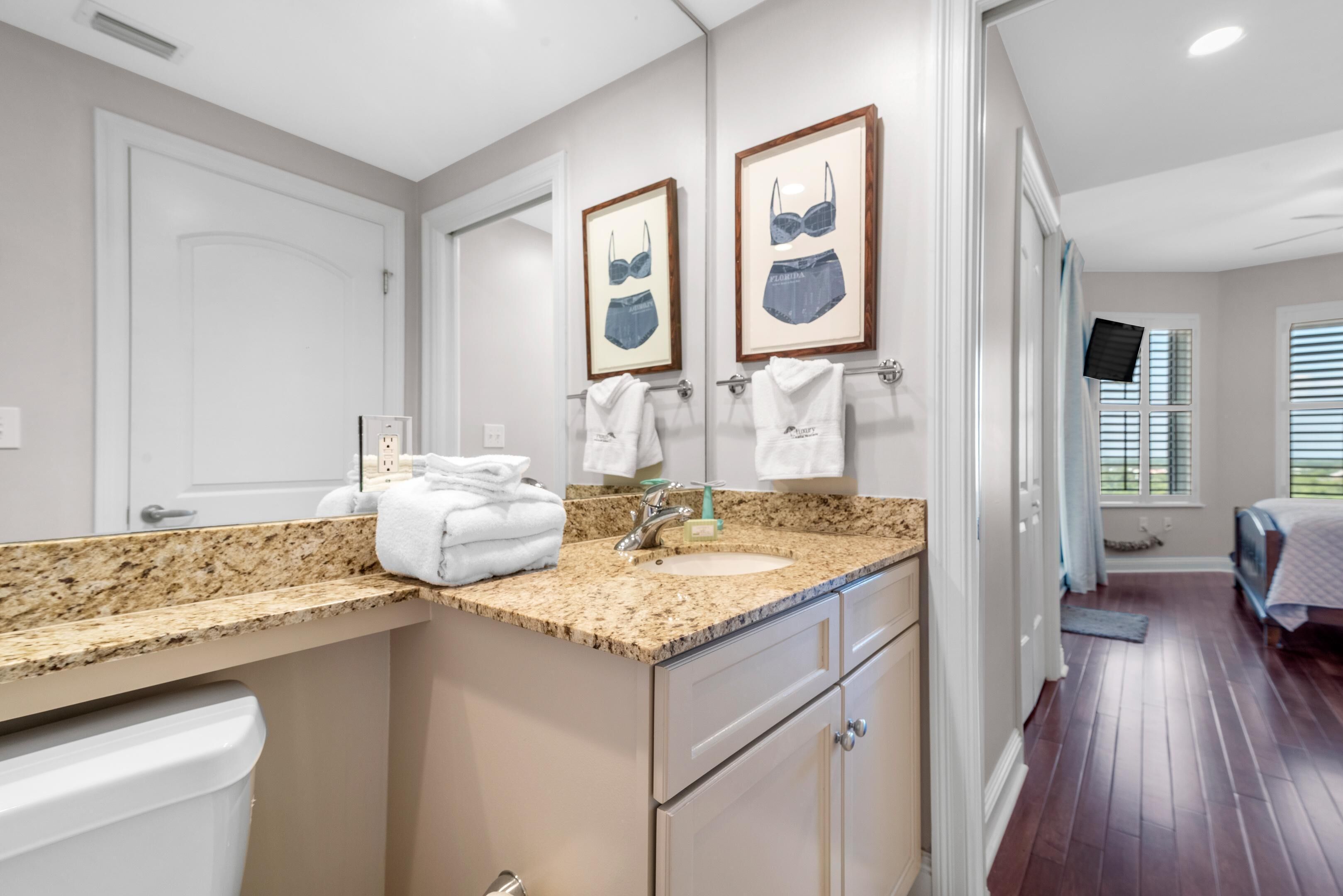 A bathroom with a granite countertop, a sink, a toilet, and framed artwork on the wall.