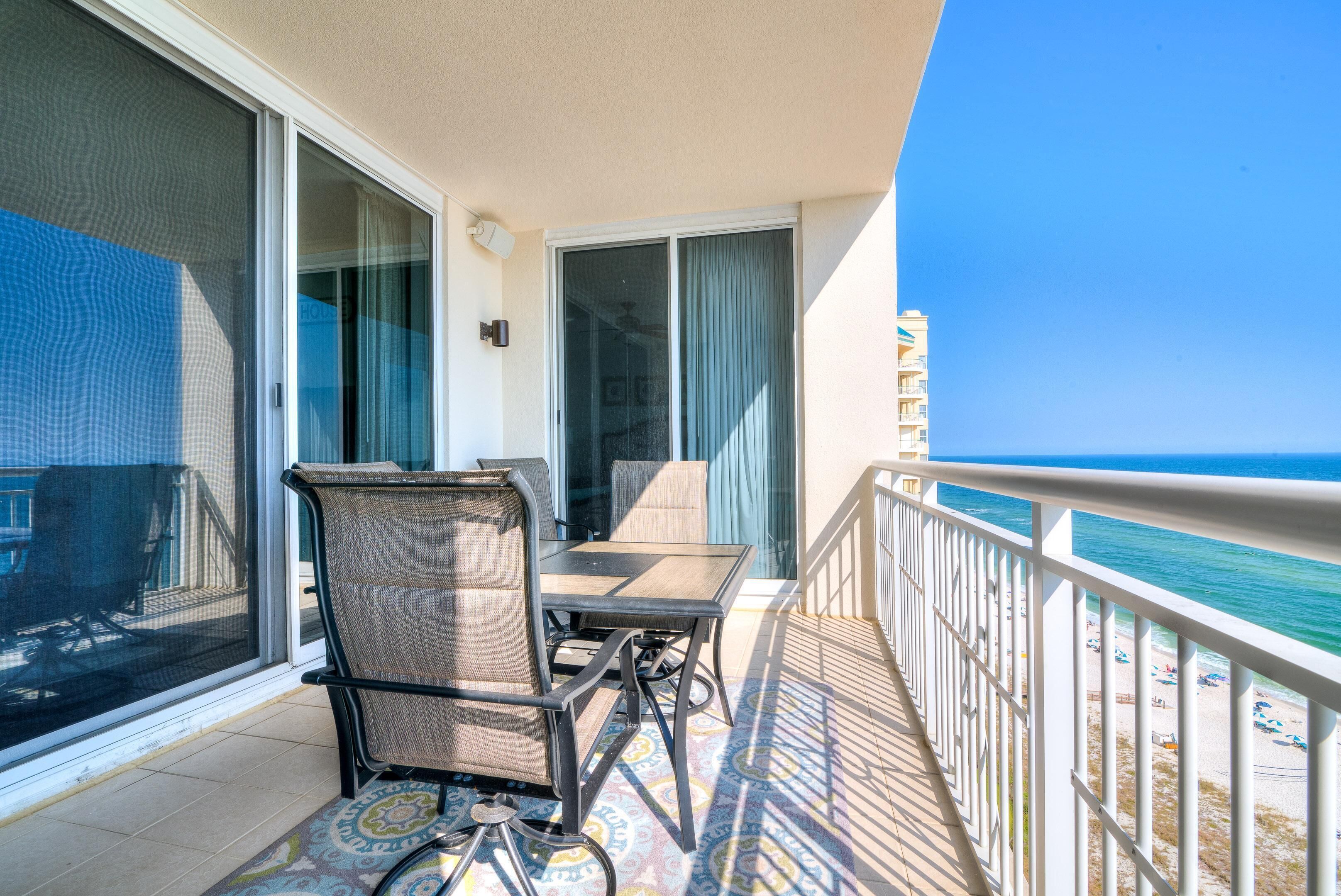 A balcony with a table and chairs, a view of the ocean, and a building in the background.