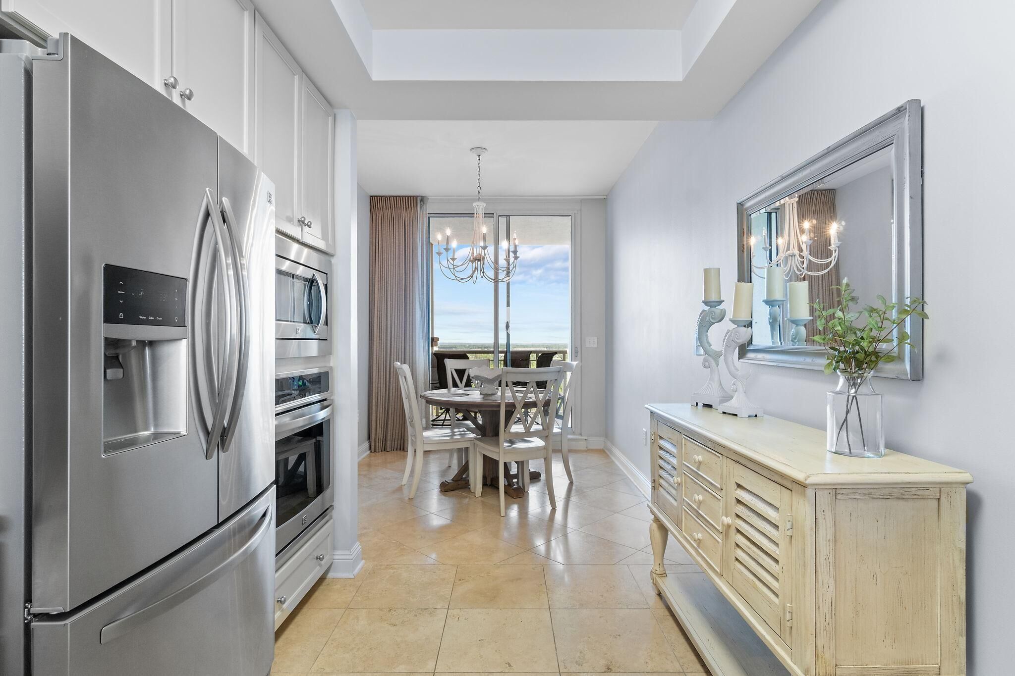 A modern kitchen with stainless steel appliances, a dining area with a chandelier, and a large mirror on the wall.
