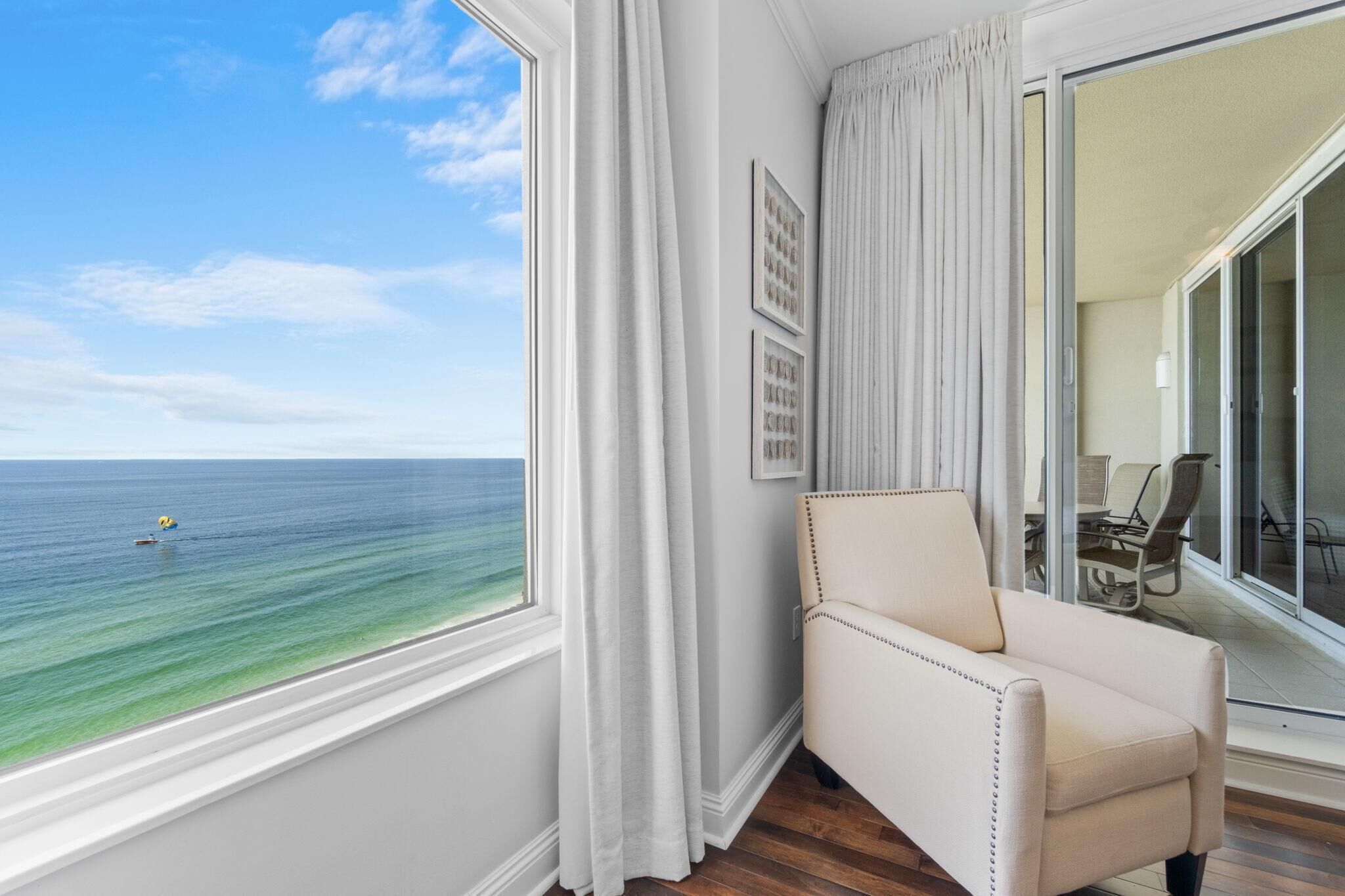 Una habitación con vista al océano, una silla blanca y un área de comedor con sillas y una mesa.