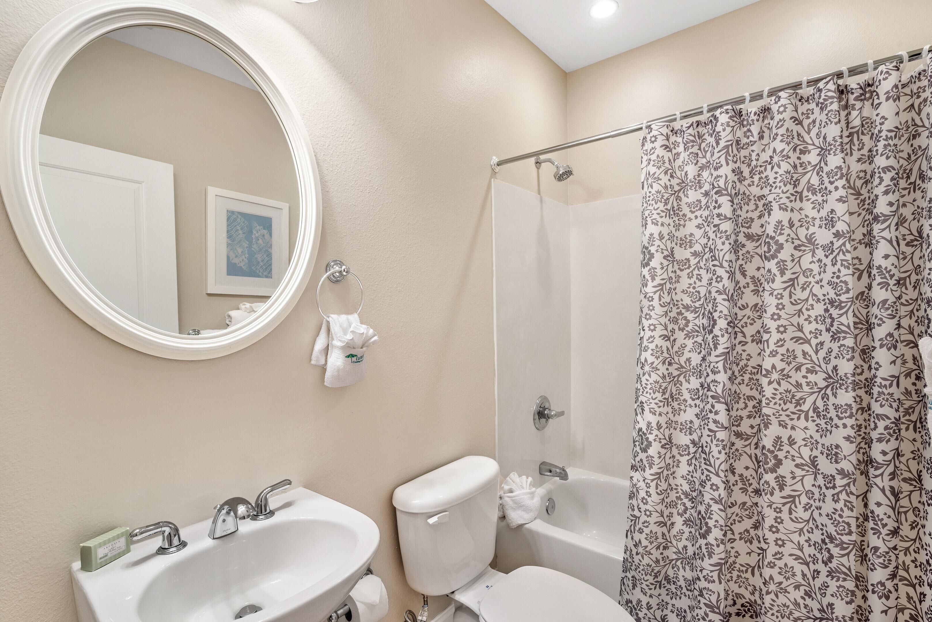 Een badkamer met een ronde spiegel, een wastafel, een toilet en een douche met bloemen gordijnen.