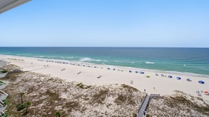 A beach view with a clear sky, sandy beach, and umbrellas. - Seaspray East 1023- Gulf Front (Pensacola)