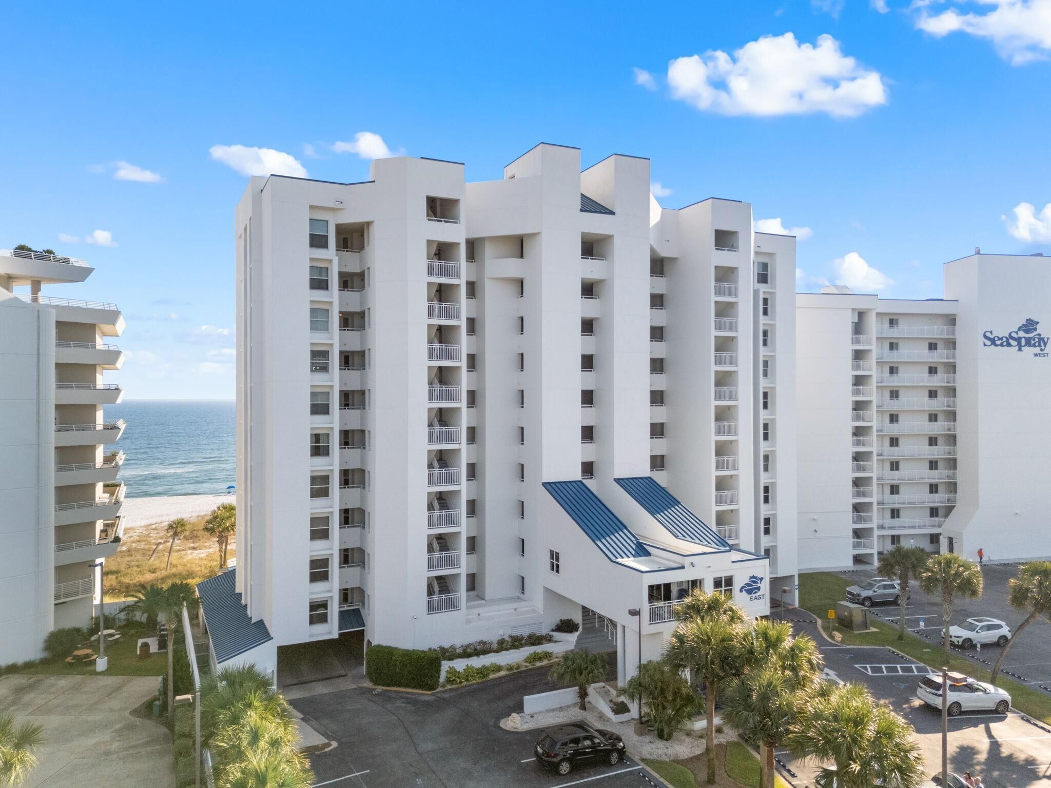 A multi-story hotel with balconies, a parking area, and a view of the ocean.
