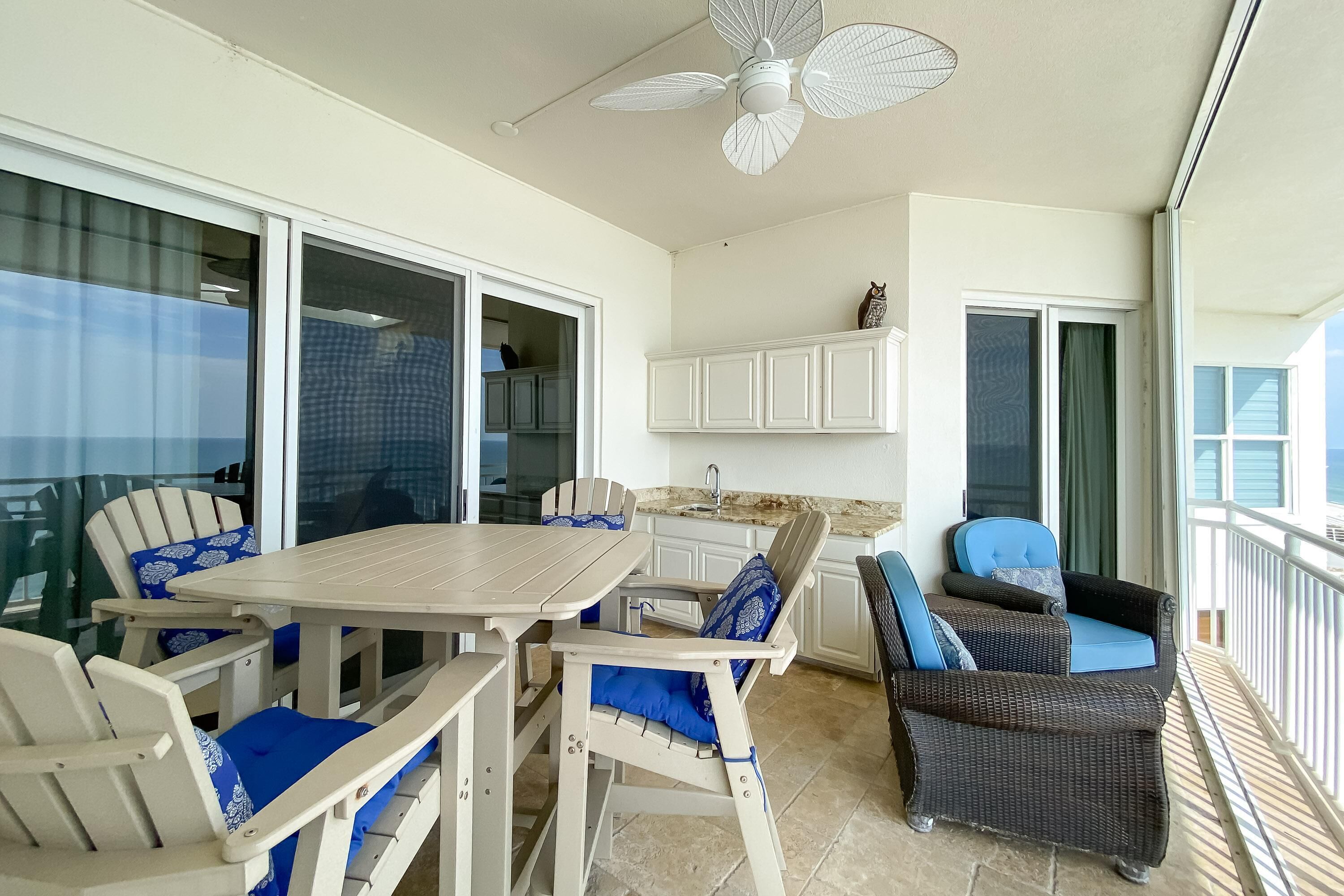 A covered outdoor area with a table and chairs, a ceiling fan, and a view of the ocean.