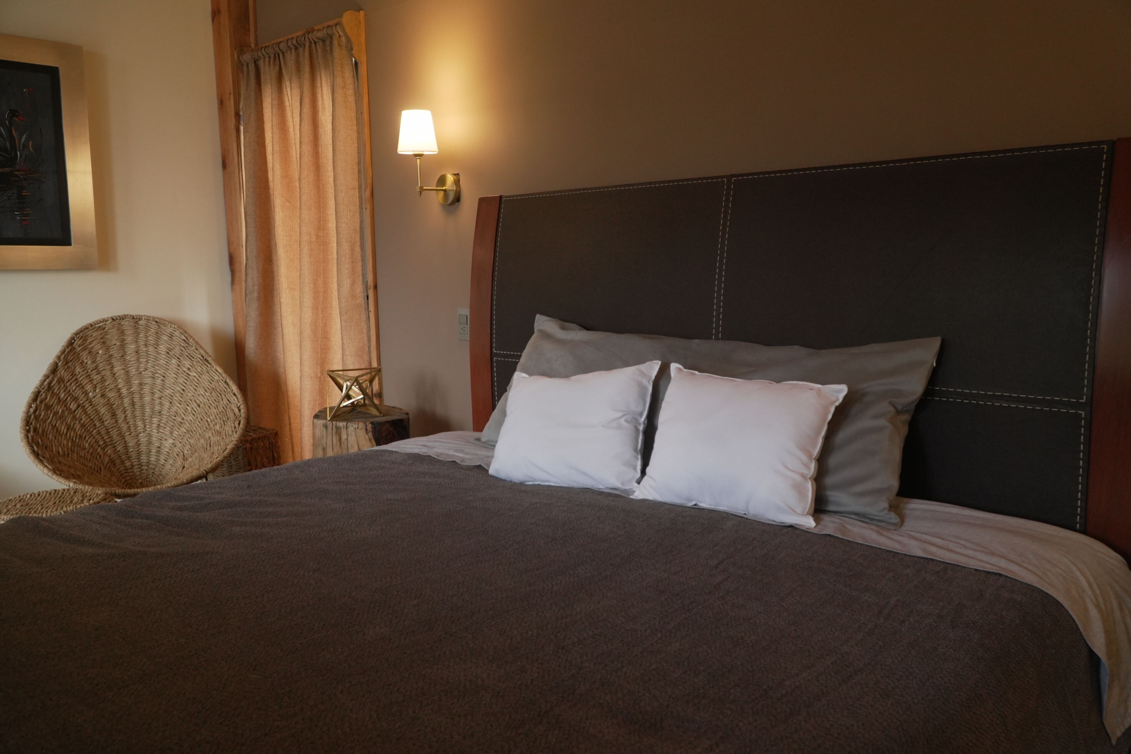 A neatly made bed with a dark headboard, a bedside lamp, and a woven chair.