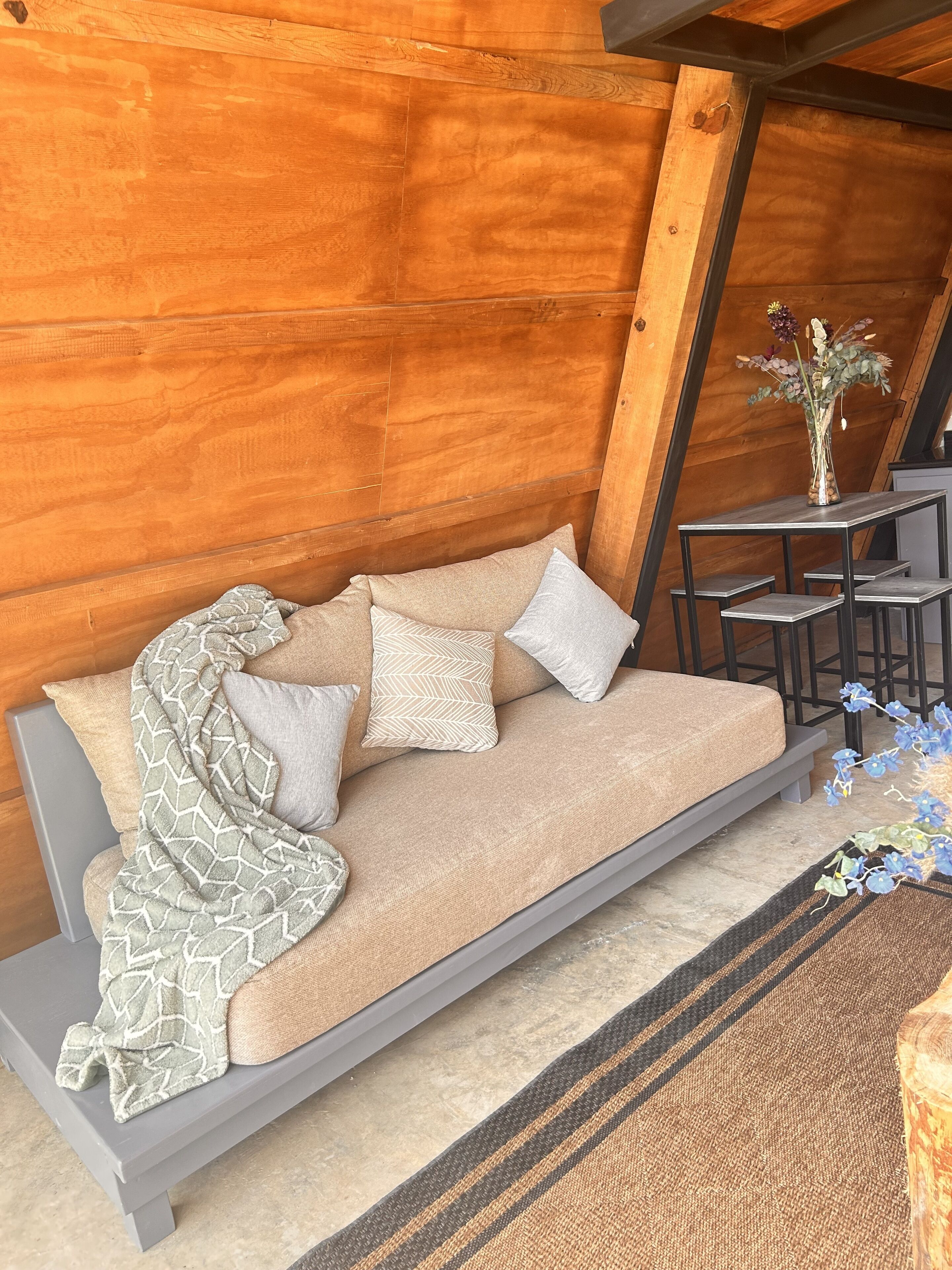 A cozy wooden cabin interior with a sofa, pillows, a small table with a vase, and a bench.