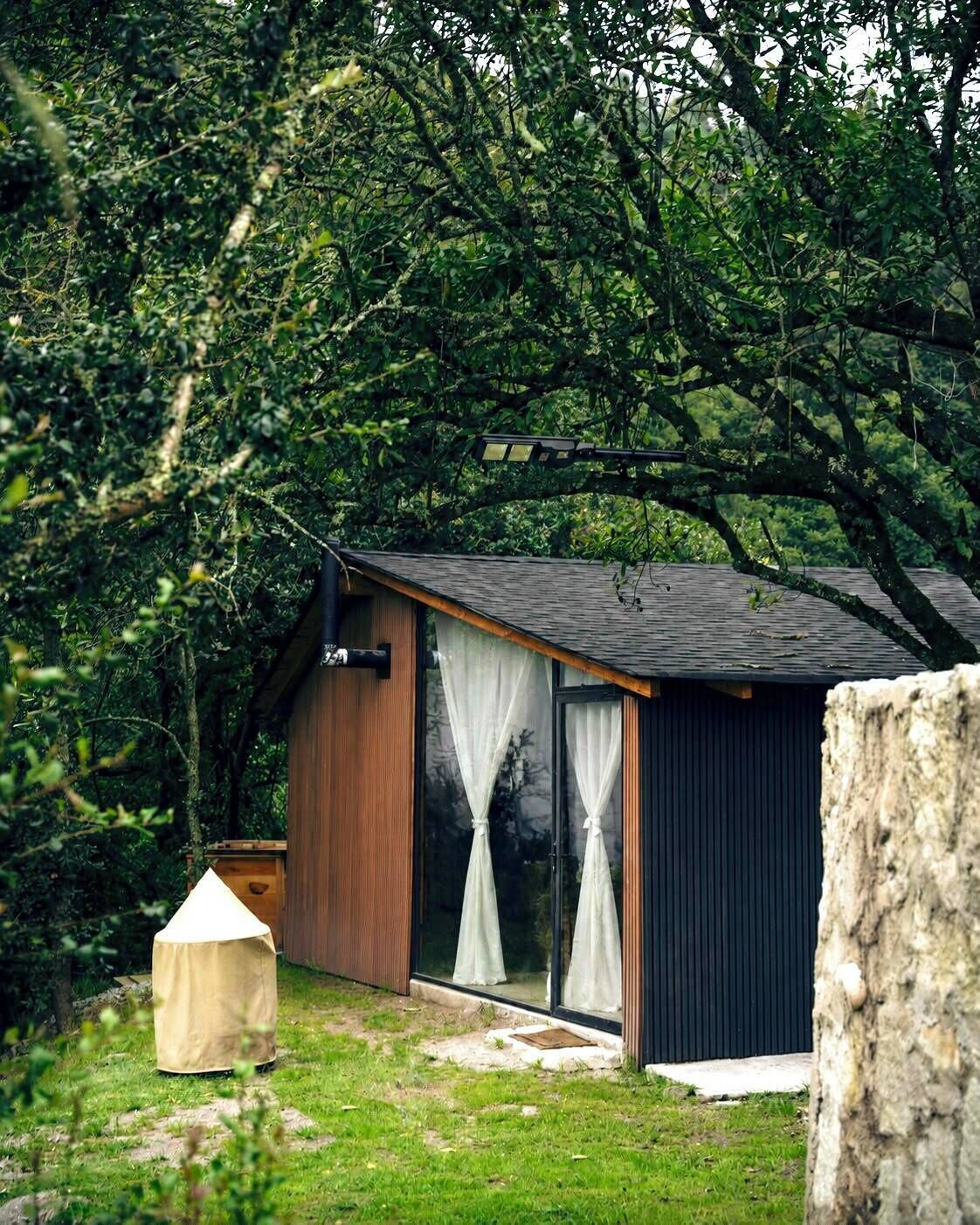 Uma cabana pequena e moderna com telhado inclinado, janelas grandes e fachada de madeira.
