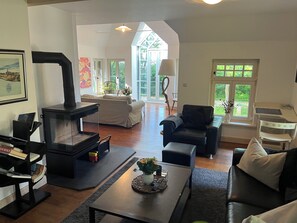 A living room with a fireplace, sofas, a coffee table, and a view through a large window.