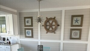 A dining area with a white table and light blue chairs, a ship's wheel, and framed nautical decorations on the wall. - 125.00 NIGHT! CONSTRUCTION SALE! NOW THRU SEPT! BEAUTIFUL JUPITER BAY 1BED 2BATH (Jupiter)