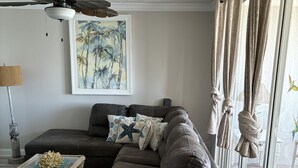 A modern living room with a sectional sofa, a glass coffee table, and a ceiling fan. - 125.00 NIGHT! CONSTRUCTION SALE! NOW THRU SEPT! BEAUTIFUL JUPITER BAY 1BED 2BATH (Jupiter)