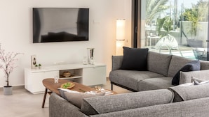 Ein modernes Wohnzimmer mit Flachbildfernseher, einer Couch, einem Couchtisch und einem Essbereich mit einem weißen Schrank.