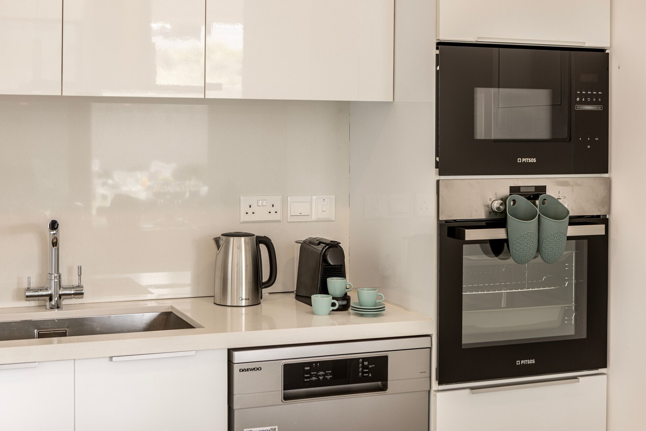 A modern kitchen with a dishwasher, coffee maker, kettle, and oven.