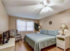 Ein Schlafzimmer mit Bett, Stuhl, Nachttisch, Lampe und Deckenventilator.