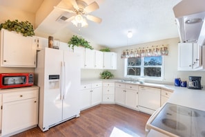 A kitchen with white cabinets, a microwave, a refrigerator, a dishwasher, and a ceiling fan.