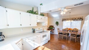 Une cuisine avec des meubles blancs, un fourneau et un coin repas comprenant des chaises et une table en bois.