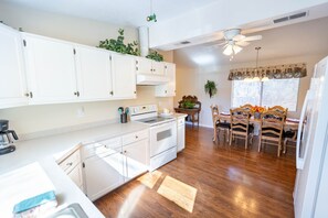 A kitchen with white cabinets, a stove, and a dining area with wooden chairs and a table. - The Hideaway at Hills Haven (Wimberley)