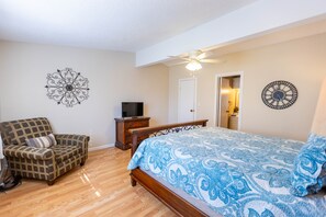 A bedroom with a wooden bed, a plaid armchair, a television, and a ceiling fan.