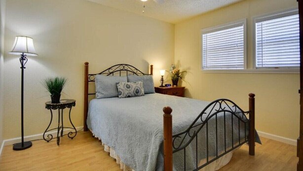 A bedroom with a bed, a ceiling fan, a bedside table with a lamp, and a window with blinds.