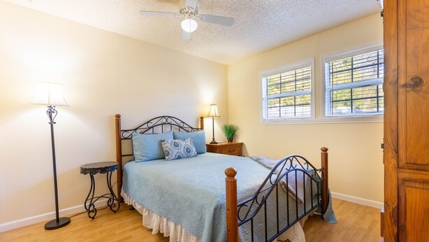 A bedroom with a bed, a nightstand, a lamp, a ceiling fan, and a window with blinds.