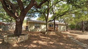 A single-story house with a stone foundation, a front porch, and a large tree in the foreground.