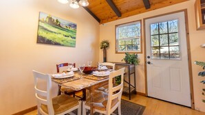 A dining area with a wooden table set for four, a painting on the wall, and a door with windows.