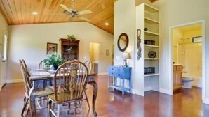 A dining area with a wooden ceiling, a dining table with chairs, and a bookshelf.