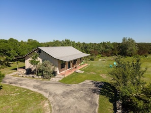 A single-story building with a sloped roof, a porch with outdoor seating, and a paved driveway. - Star Ranch Cottage- Starry Nights & Cozy Comfort (Wimberley)