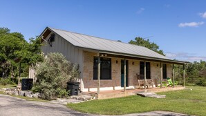 A single-story building with a gabled roof, a porch with chairs, and a stone foundation.