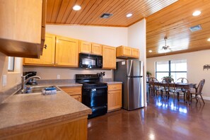 A modern kitchen with wooden cabinets, stainless steel appliances, and a dining area with a wooden table and chairs. - Star Ranch Cottage- Starry Nights & Cozy Comfort (Wimberley)