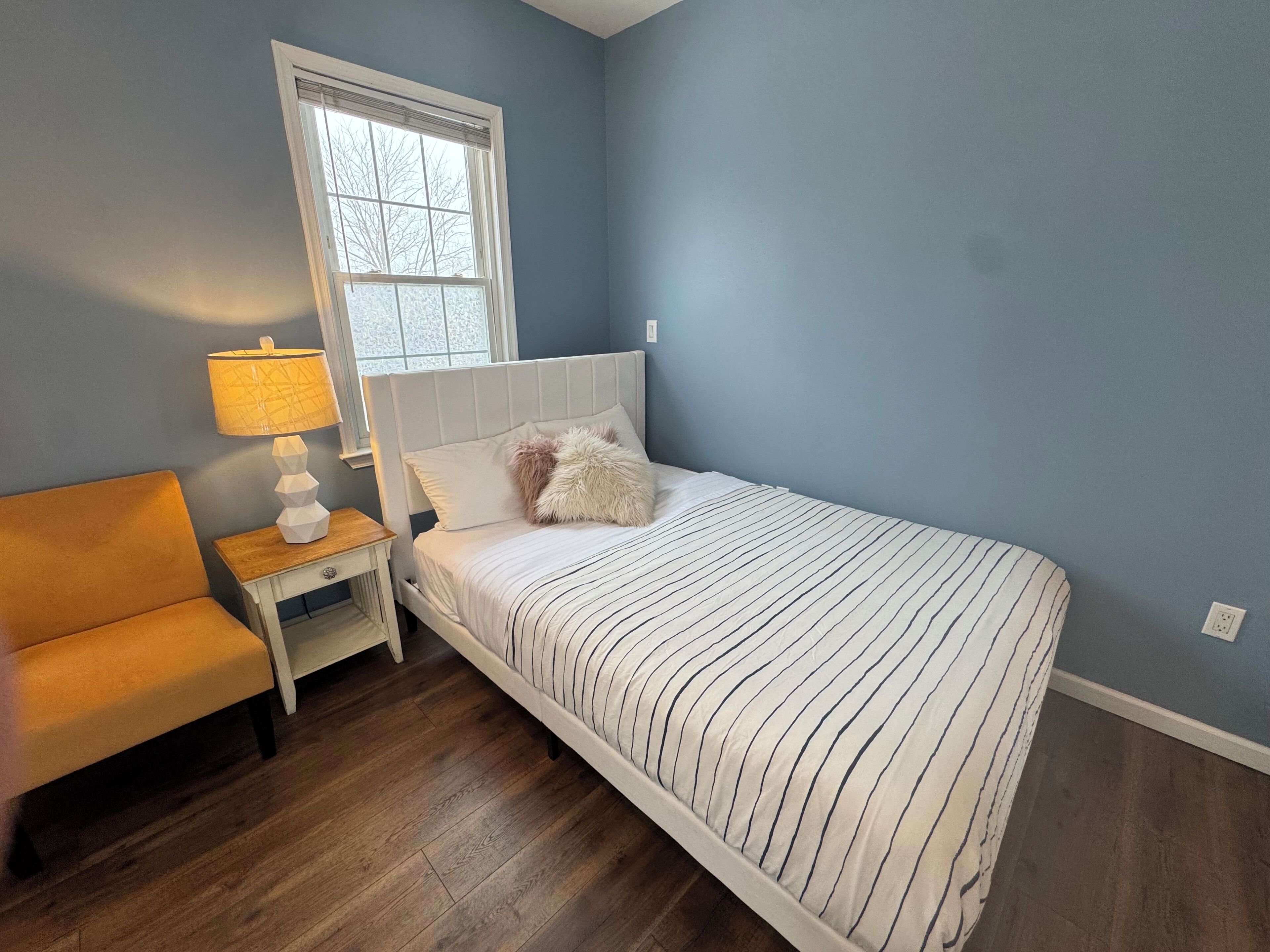 Une chambre à coucher avec un lit, une table de chevet, une lampe et une chaise.