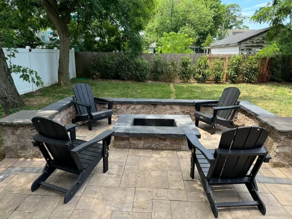 An outdoor seating area with four Adirondack chairs and a stone fire pit.