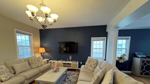 A living room with two sofas, a coffee table, a TV, and a chandelier. - Beach Mansion • 1 Block to Beach • Sleeps 16+ • Large Groups & Family Trips (Keansburg)