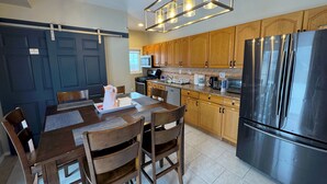 A modern kitchen with wooden cabinets, stainless steel appliances, and a dining area with a table and chairs. - Beach Mansion • 1 Block to Beach • Sleeps 16+ • Large Groups & Family Trips (Keansburg)