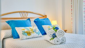 Ein ordentlich gemachtes Bett mit blauen Kissen, einem Blumenkissen und Blüten-gerollten Handtüchern.