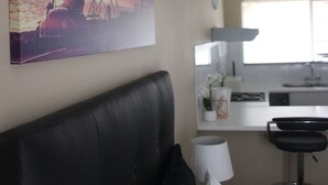 A hotel room with a bed, a painting on the wall, a kitchen area, and a window.
