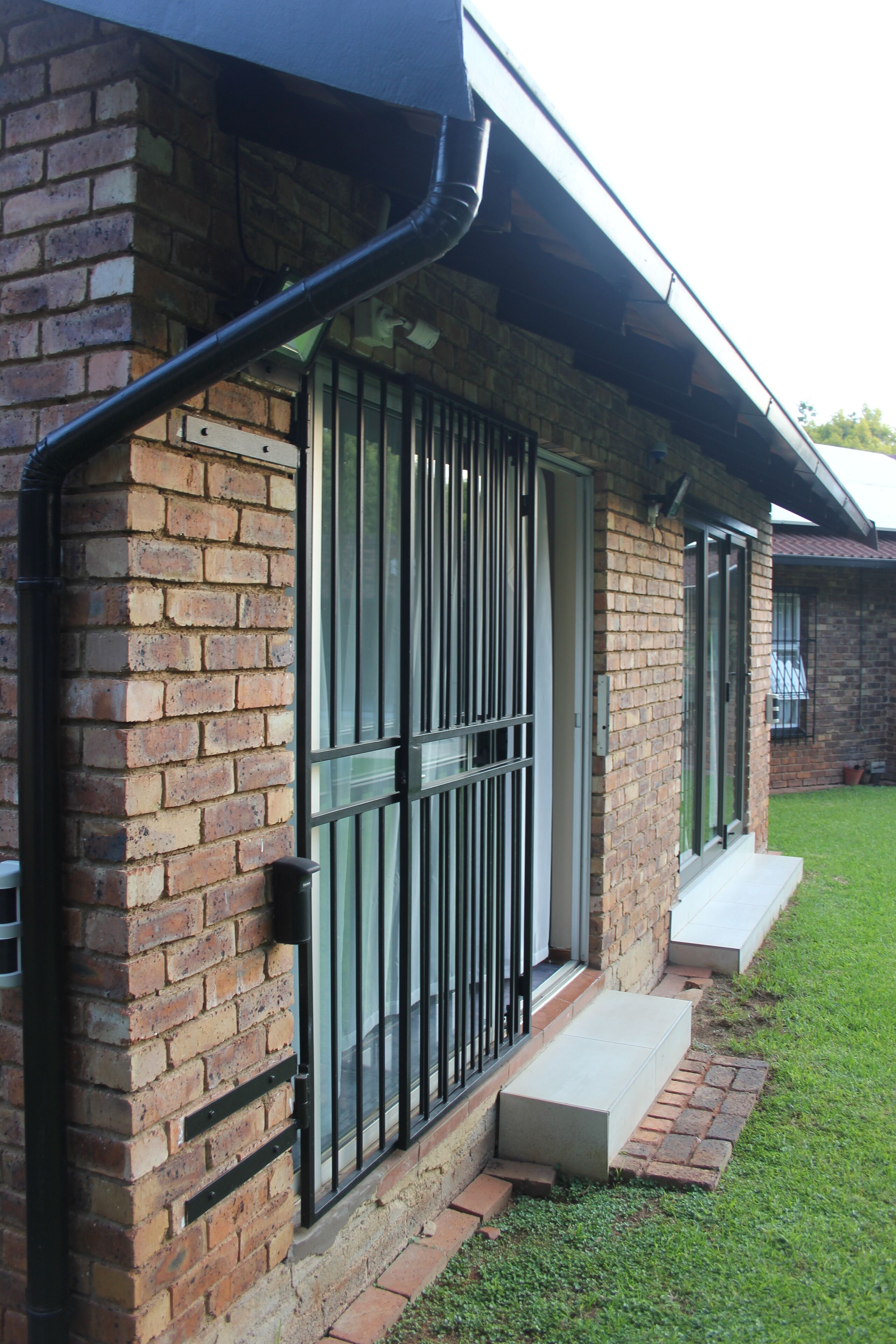 A brick building with a metal gate, a small concrete step, and a grassy yard.