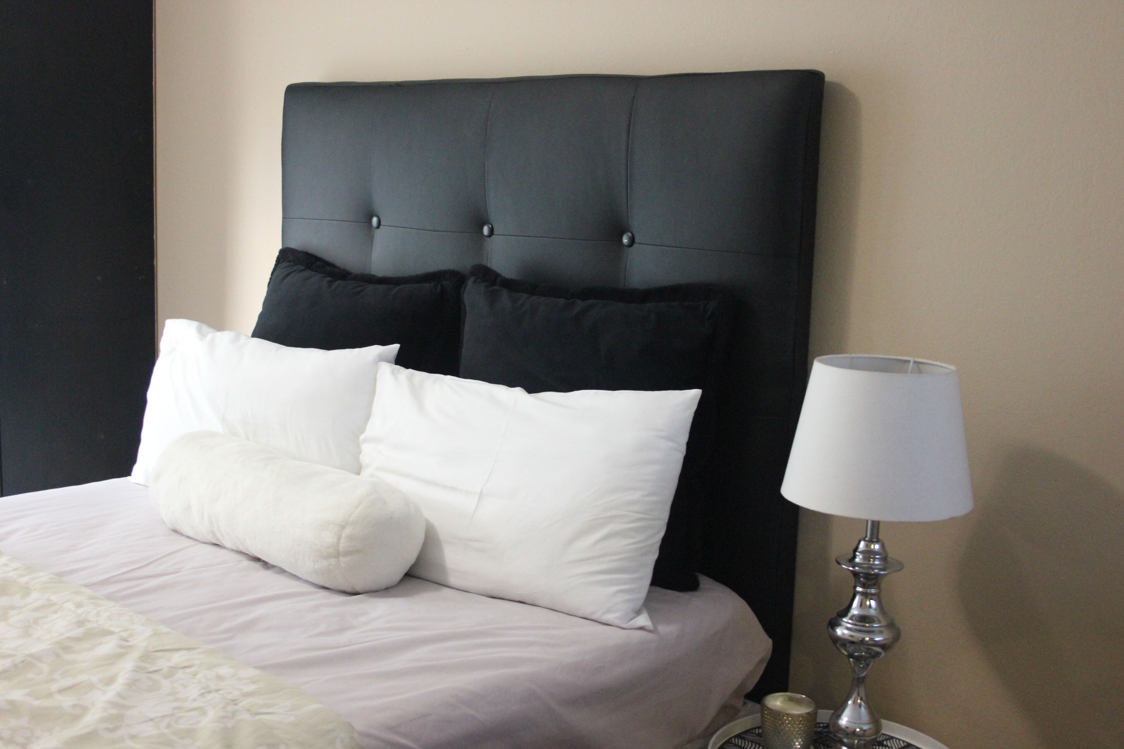 A bed with a black headboard, white and black pillows, and a bedside table with a lamp and a candle.