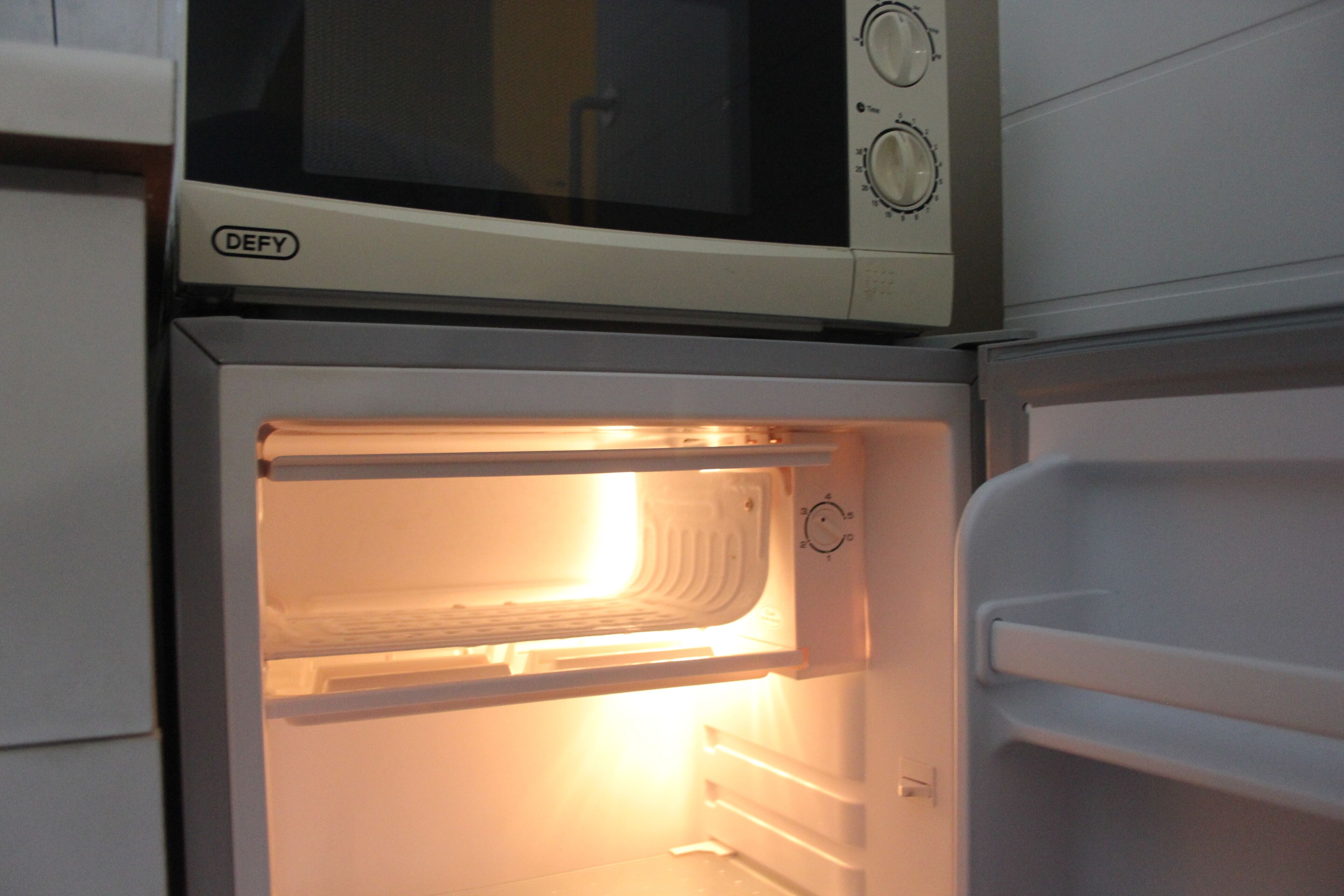An open refrigerator with a microwave on top.