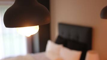 A close-up of a lamp with a warm light, a bed with white bedding, and a dark headboard in a hotel room.