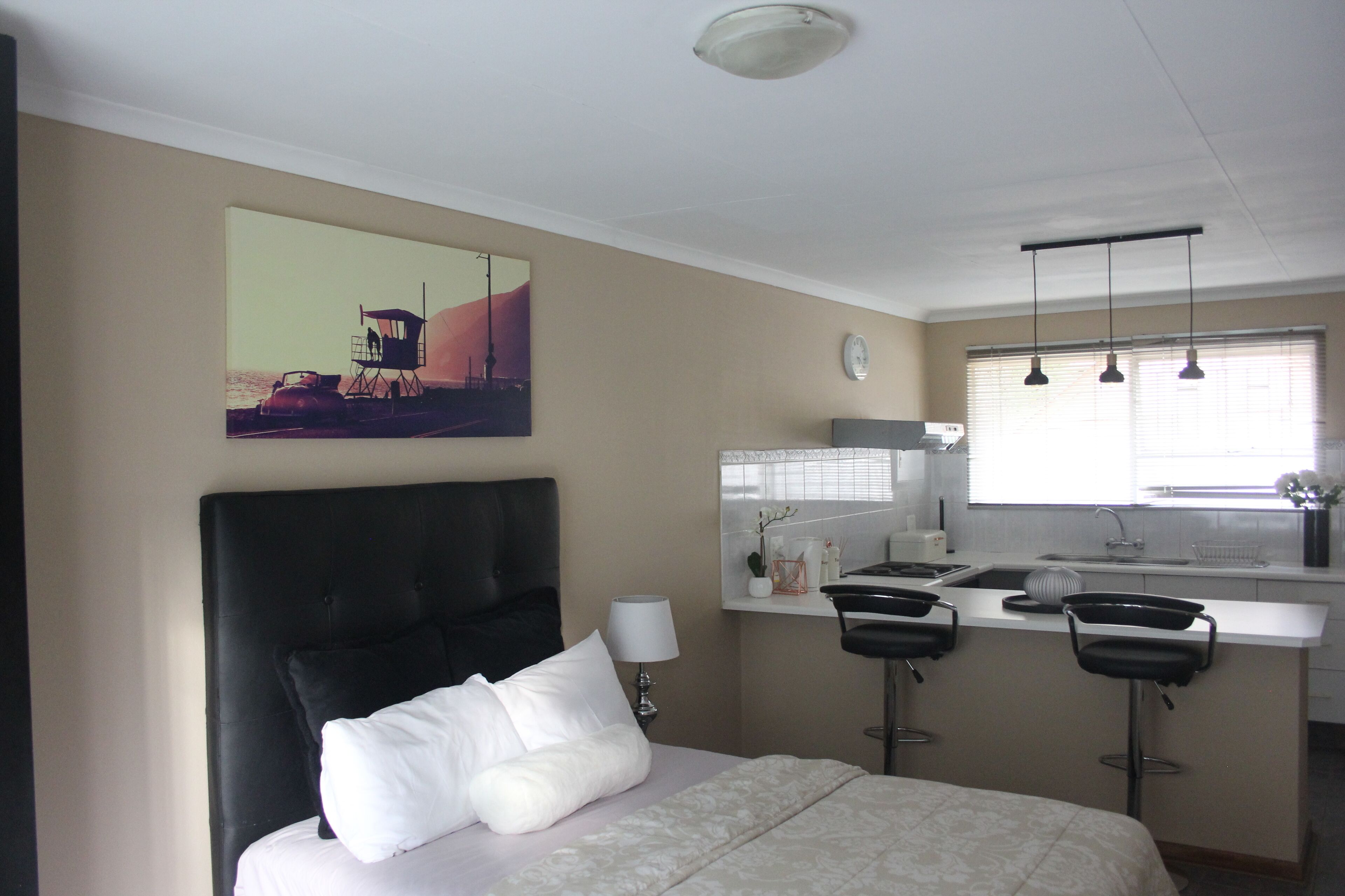 A hotel room with a large bed, a small kitchenette, and a dining area with two bar stools.