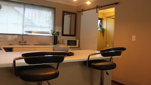 A kitchen with a white countertop, a microwave, a sink, and two black bar stools.