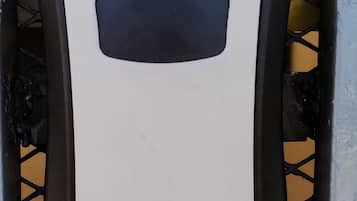 Un objet rectangulaire blanc, surmonté d’une partie noire, qui pourrait être un panneau de commande ou un appareil, fixé sur un cadre métallique dont le fond présente un motif en losanges.