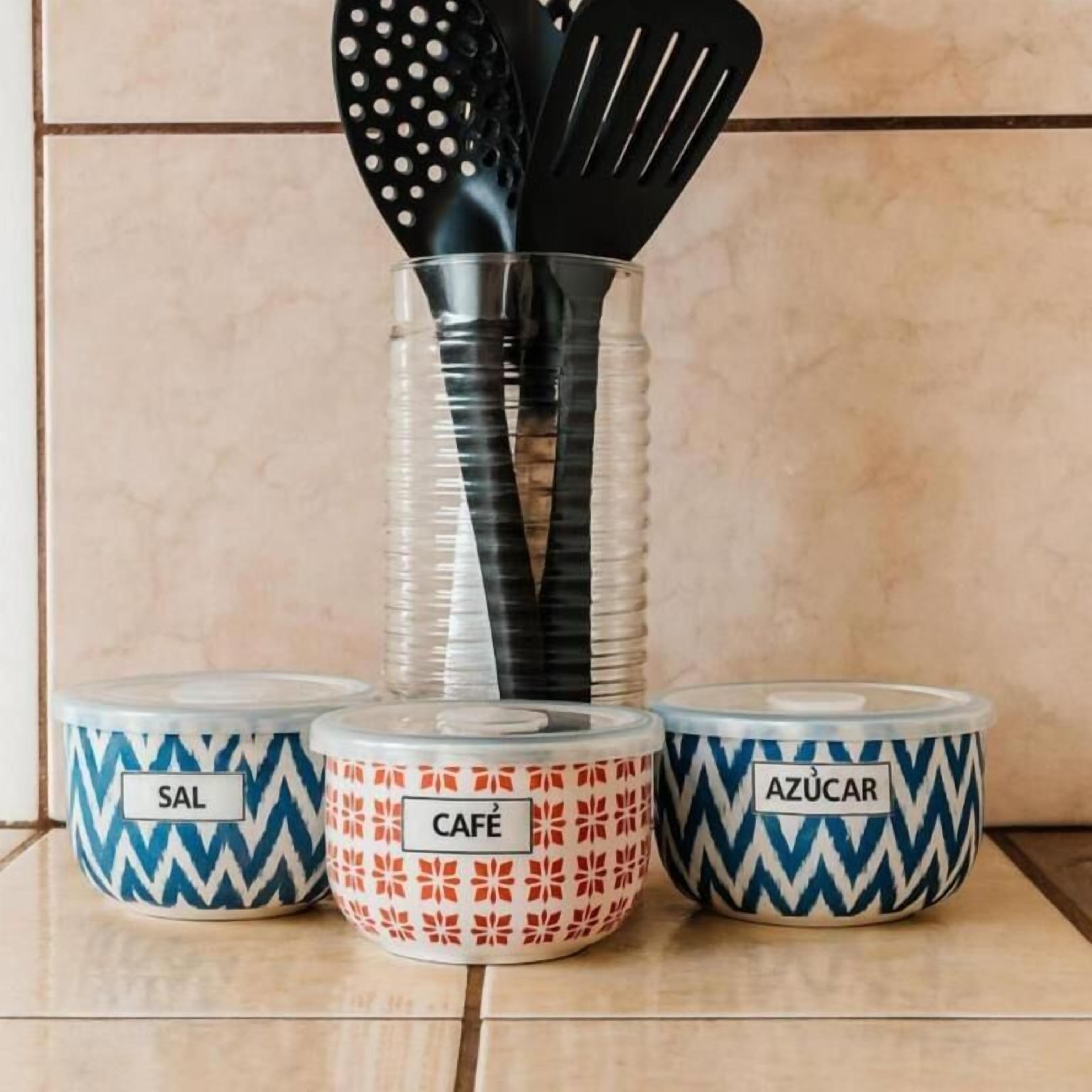 Three kitchen spice jars labeled 'SAL', 'CAFE', and 'AZÚCAR' with black spatulas inserted into the 'CAFE' jar.