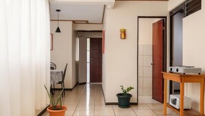 A hallway with a dining area, a potted plant, a microwave, and a wooden table. - Casa Cafetal Aeropuerto (Alajuela)