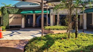 An outdoor area with a restaurant named 'Los Artijitos', featuring a covered seating area, a small garden with flowers, and a clear sky. - Casa Cafetal Aeropuerto (Alajuela)