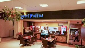 A restaurant named 'CostiPollos' with a counter, seating area, and a person walking in the background. - Casa Cafetal Aeropuerto (Alajuela)